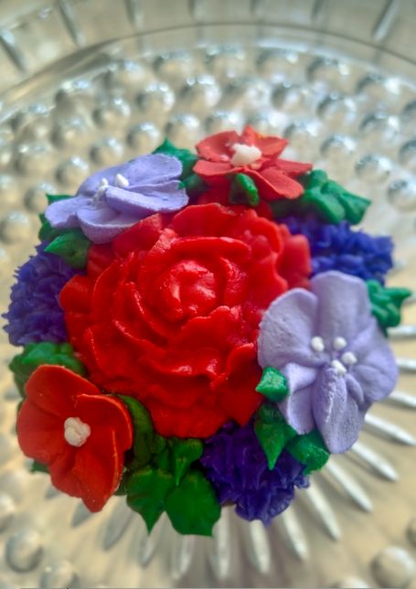 Elaborately decorated cupcake with a mix of purple and red flowers.  Perfect for a Red Hat Society gathering.